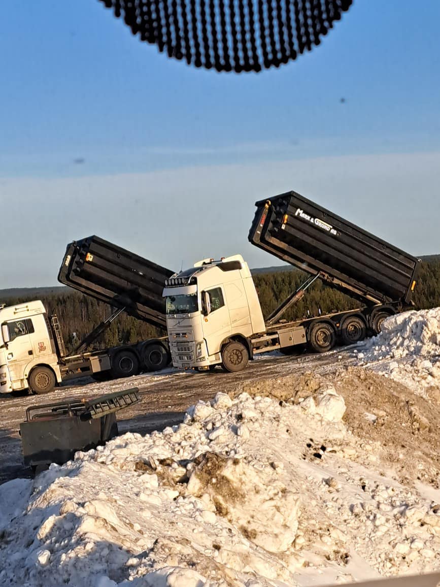 Vit lastbil med svart grusflak i vintermiljö.